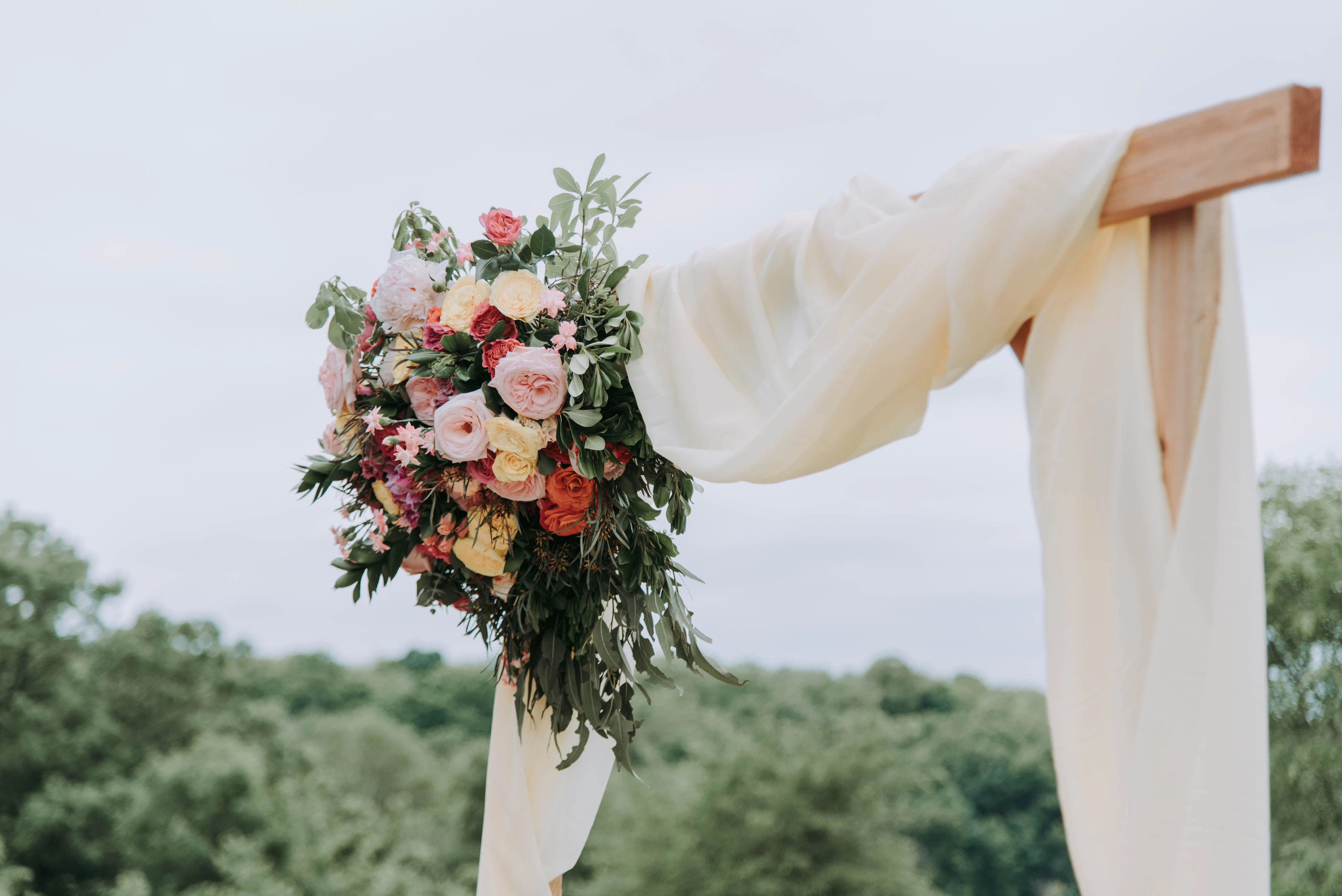A minimal ceremony arch dressed in soft florals against an open Tuscan sky