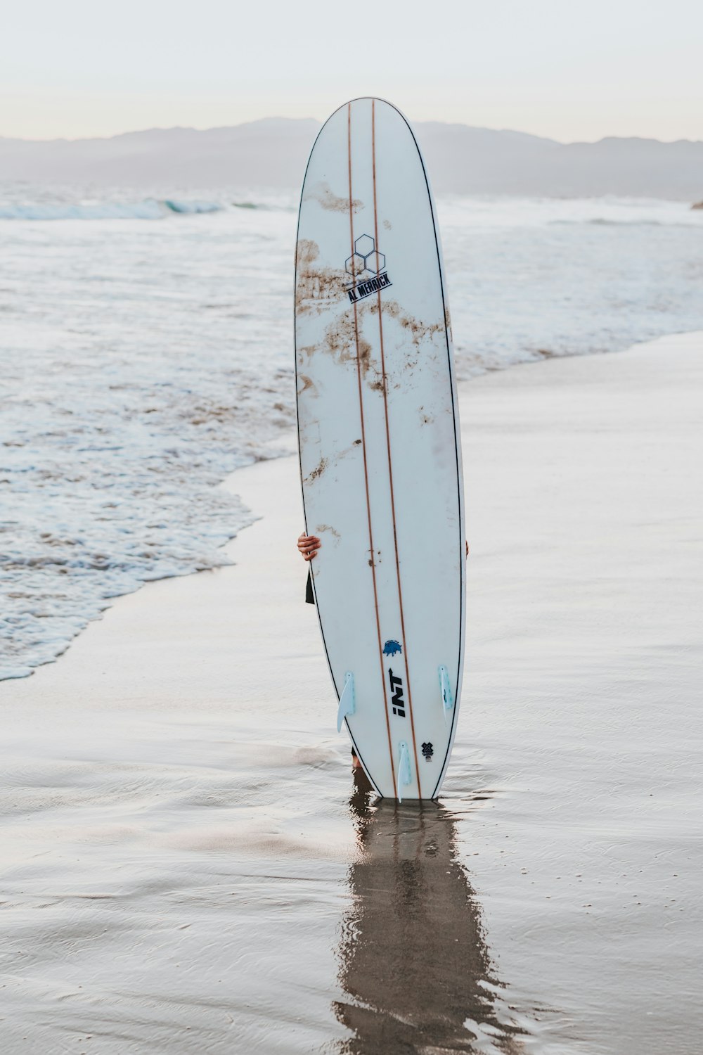 white surfboard upright on seashore during daytime