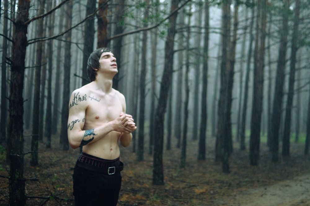 man wearing black bottoms standing surrounded by tall trees during daytime