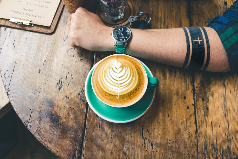 cappuccino next to man's arm whose wearing watch