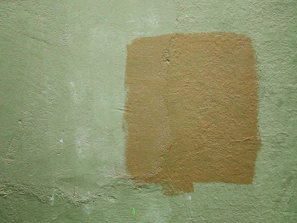 Artist applying textured plaster on a wall with green khaki accents in a cozy room.