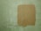 A textured wall with a light green color and a rectangular patch of a darker tan paint applied over it. The paint appears uneven, adding a rough texture to the surface.