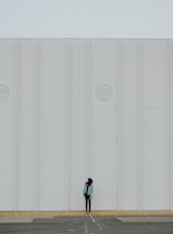 A minimalist black and white photo of a lone figure standing against an industrial backdrop.