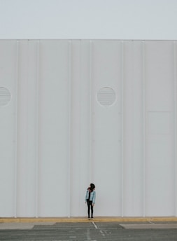 A minimalist black and white photo of a lone figure standing against an industrial backdrop.