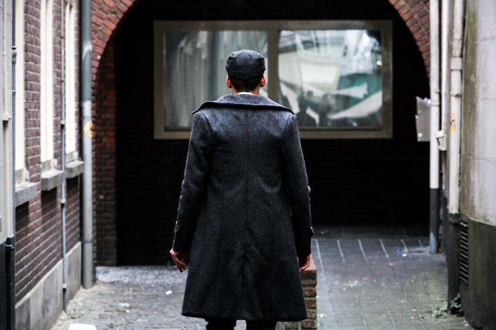 Person in schwarzem langen Mantel steht in der Nähe eines klaren Glasfensters