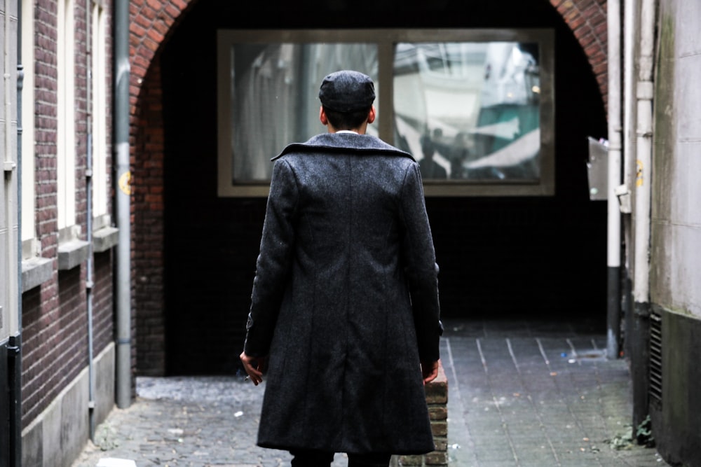 personne en manteau long noir debout près d’une fenêtre en verre clair