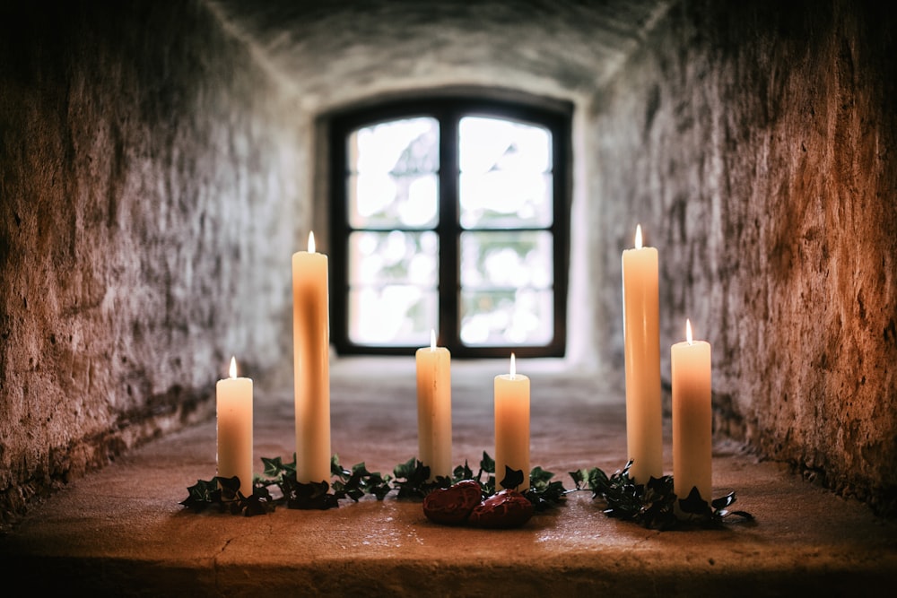 Sechs weiße, sich verjüngende Kerzen stehen auf grauem Betonpflaster im Raum