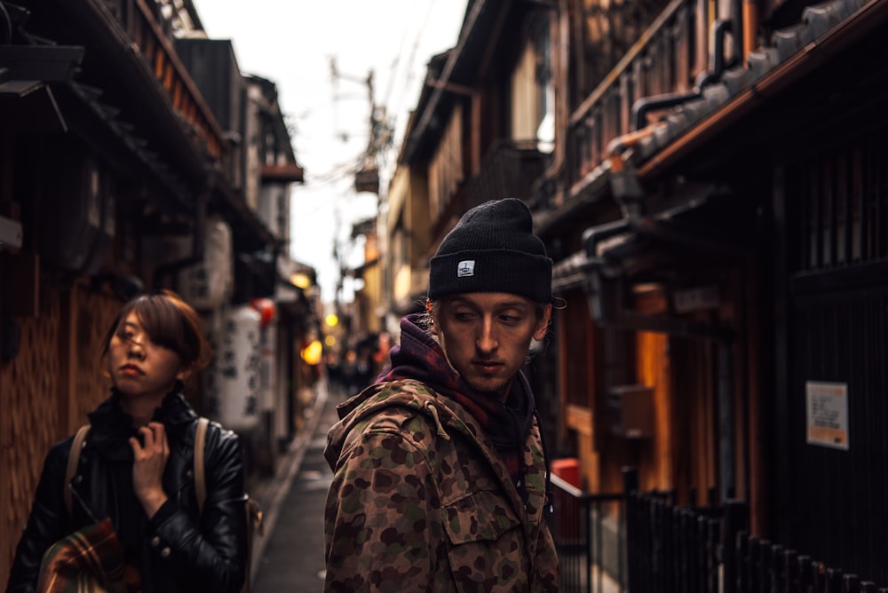 Femme en veste de camouflage marron et vert et casquette en tricot noir marchant dans la rue pendant la journée