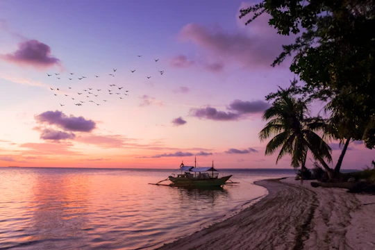 A sunset view over Gili Trawangan's white sandy beach with colorful boats anchored near shore.