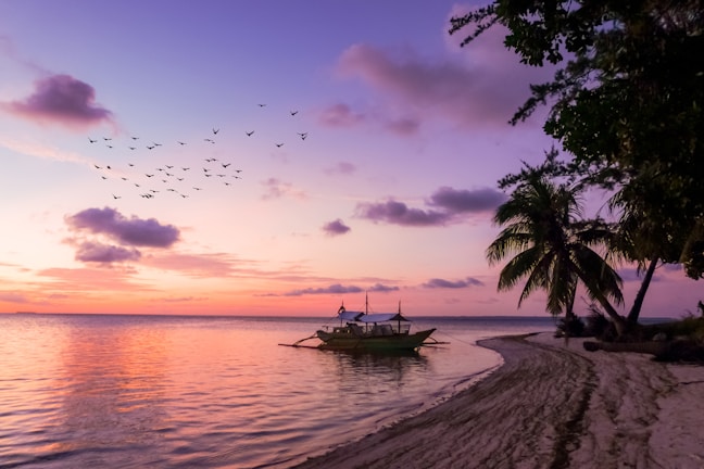 A vibrant sunset over a tropical beach with a small boat anchored near the shore.