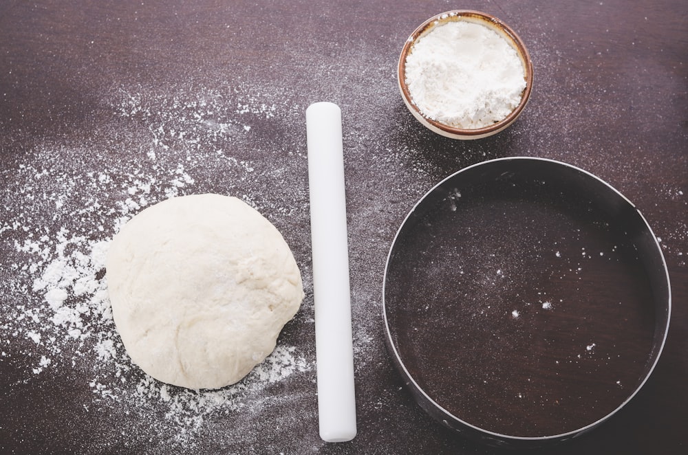 dough near white roller pin beside round baking pan