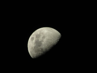 The image features a close-up view of the Moon against a black night sky. The Moon is in its waxing gibbous phase, with its surface showing visible craters and rough textures.