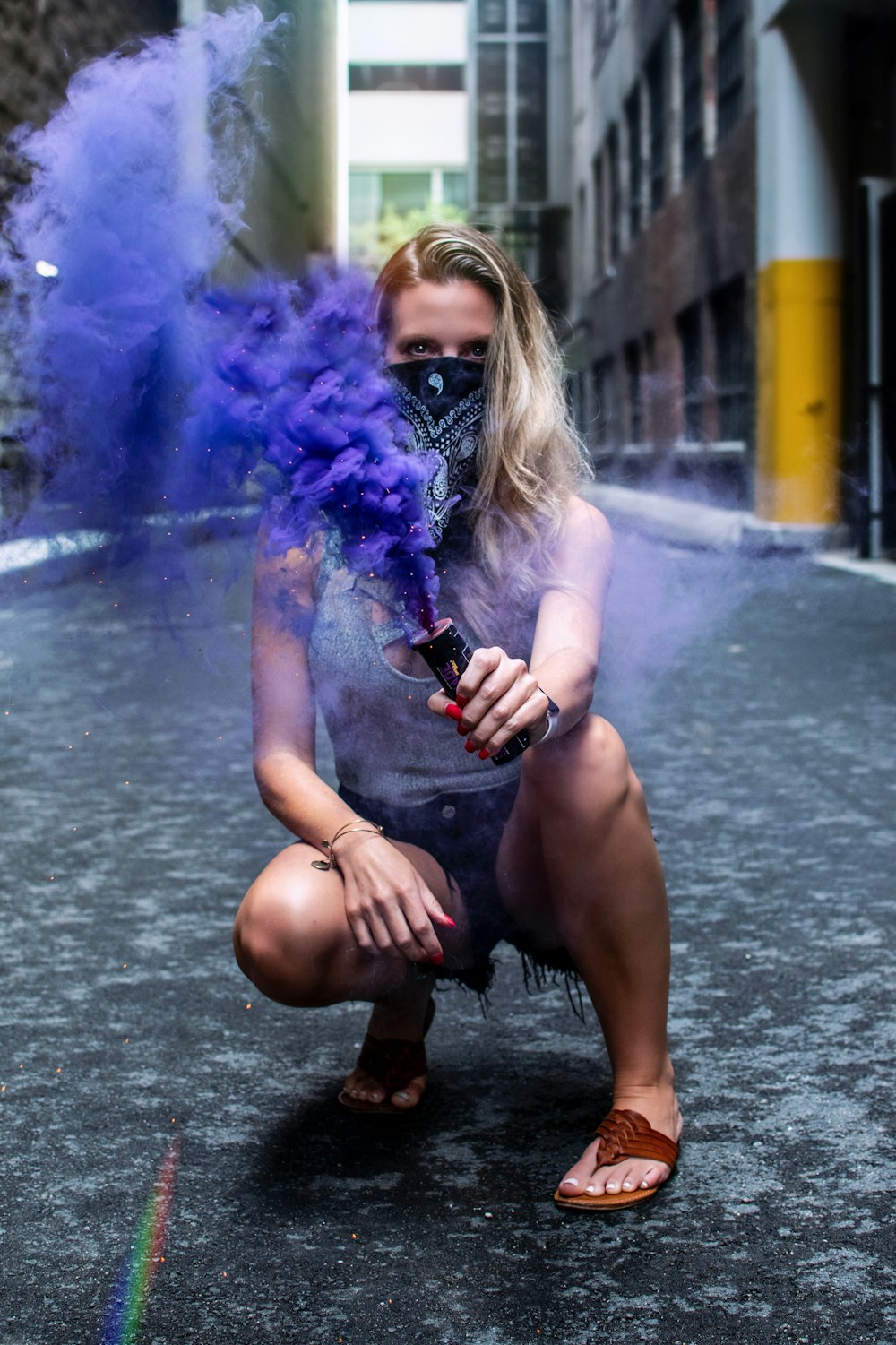 Mujer inclinada sobre el pavimento de hormigón sosteniendo humo azul