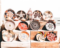 A collection of intricately woven baskets and pottery with vibrant geometric patterns displayed on wooden shelves. There is a variety of colors and designs, showcasing traditional and cultural artistry.