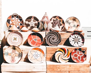 A collection of intricately woven baskets and pottery with vibrant geometric patterns displayed on wooden shelves. There is a variety of colors and designs, showcasing traditional and cultural artistry.