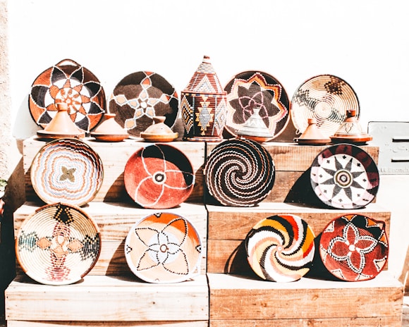 A collection of intricately woven baskets and pottery with vibrant geometric patterns displayed on wooden shelves. There is a variety of colors and designs, showcasing traditional and cultural artistry.