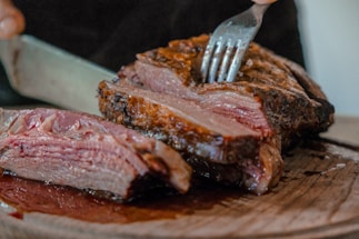 person slicing a meat on brown wooden board