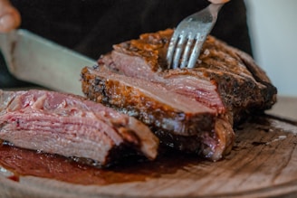 person slicing a meat on brown wooden board