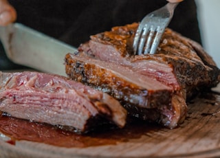 person slicing a meat on brown wooden board