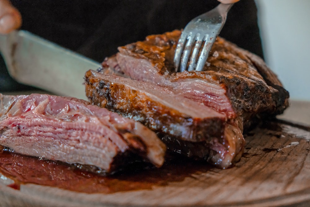 pessoa cortando uma carne em tábua de madeira marrom