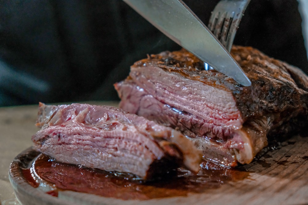 person slicing juicy medium rare meat on top of brown wooden cutting board