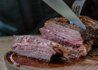 person slicing juicy medium rare meat on top of brown wooden cutting board