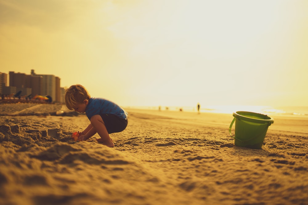 child playing on sand near pail