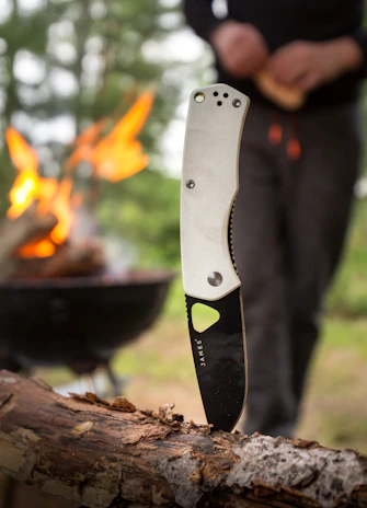 Close-up of a bushcraft knife cutting through fresh herbs beside a campfire.