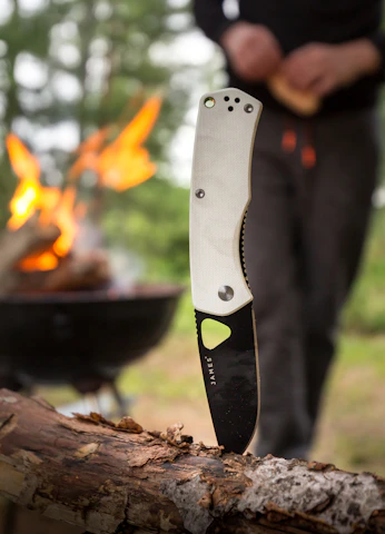Close-up of hands holding a handcrafted bushcraft knife over a campfire.