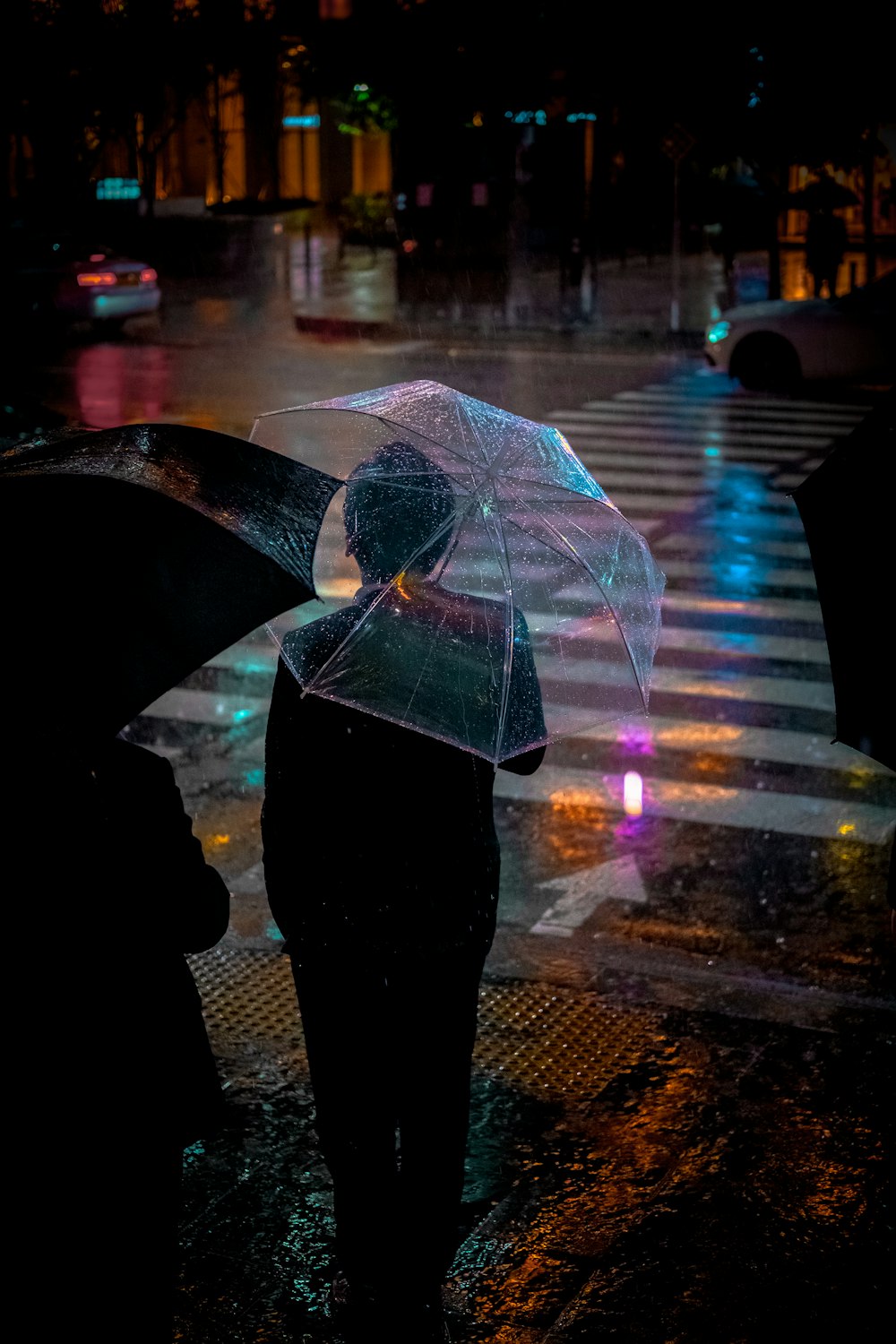 Homme vêtu d’une veste de costume noire tenant un parapluie transparent devant une voie piétonne