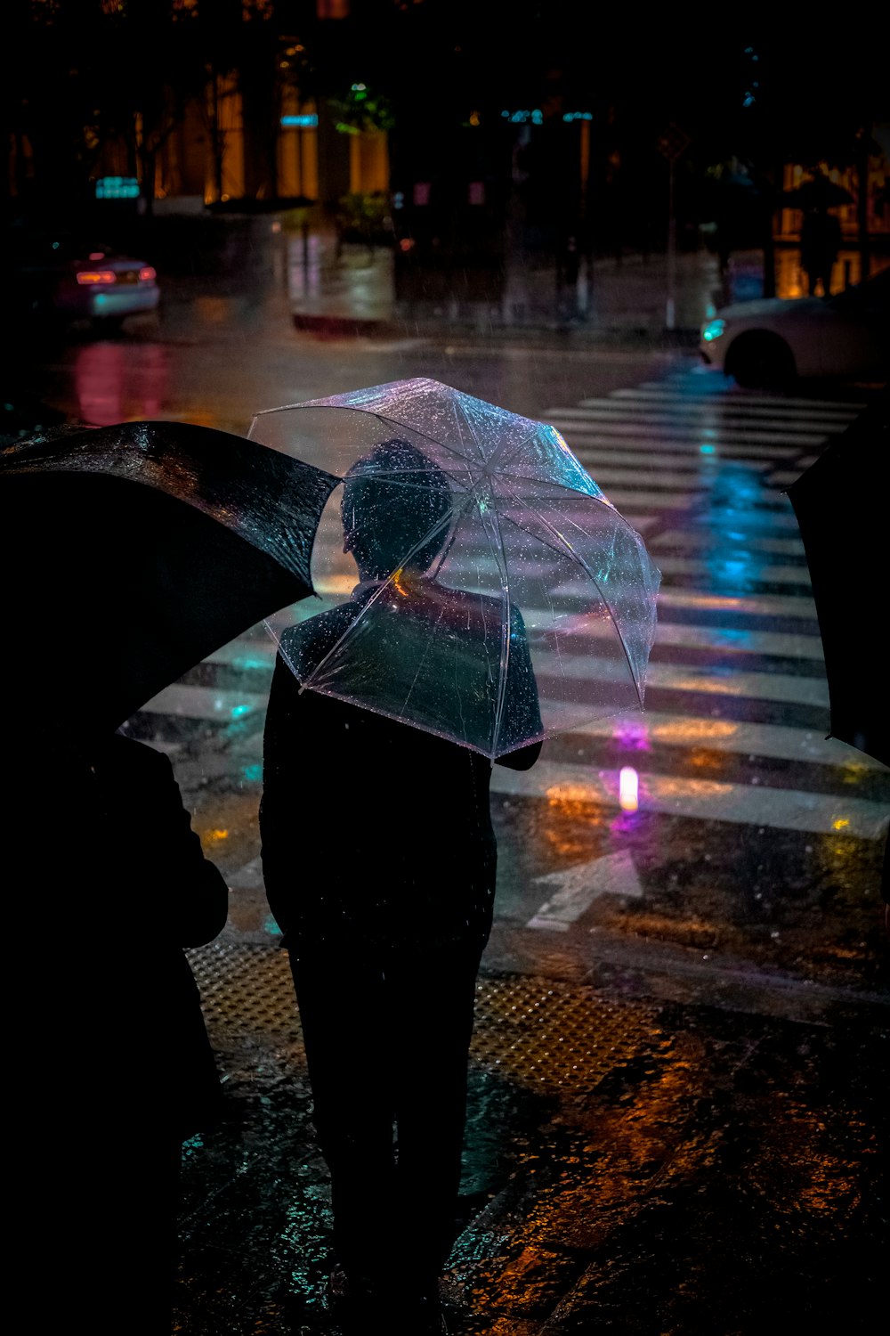 man wearing black suit jacket holding clear umbrella in front of pedestrian lane