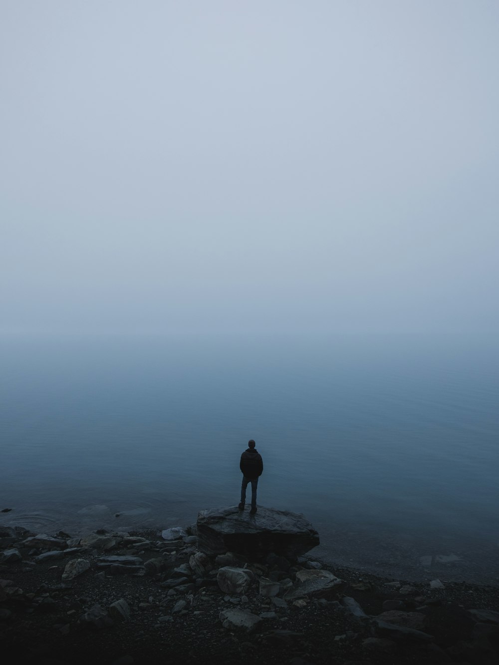 man standing on rock near body of water