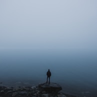 man standing on rock near body of water