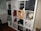 A multi-compartment shelf filled with various items including books, action figures, a globe, a red lantern, and decorative artworks. A pop art style poster of a woman holding a drink is prominently displayed, alongside Funko Pop figures and a small cactus in a white pot.