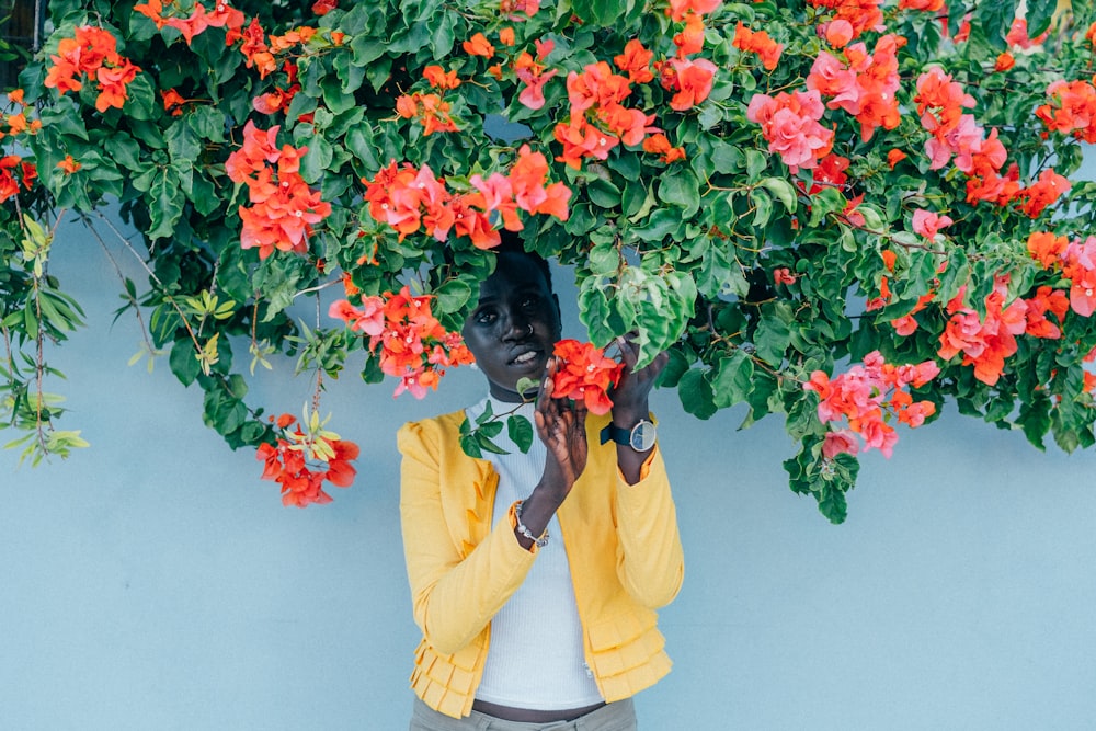 mujer de pie debajo de la flor de pétalos de naranja con la planta de hoja verde