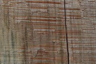 Wooden texture with horizontal grain patterns in shades of brown and beige, featuring a prominent vertical crack running through the center.
