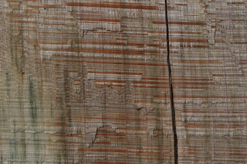 Wooden texture with horizontal grain patterns in shades of brown and beige, featuring a prominent vertical crack running through the center.
