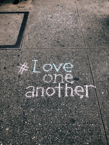 love one another chalk written on concrete floor