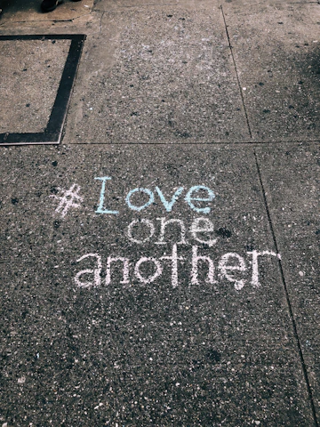 love one another chalk written on concrete floor