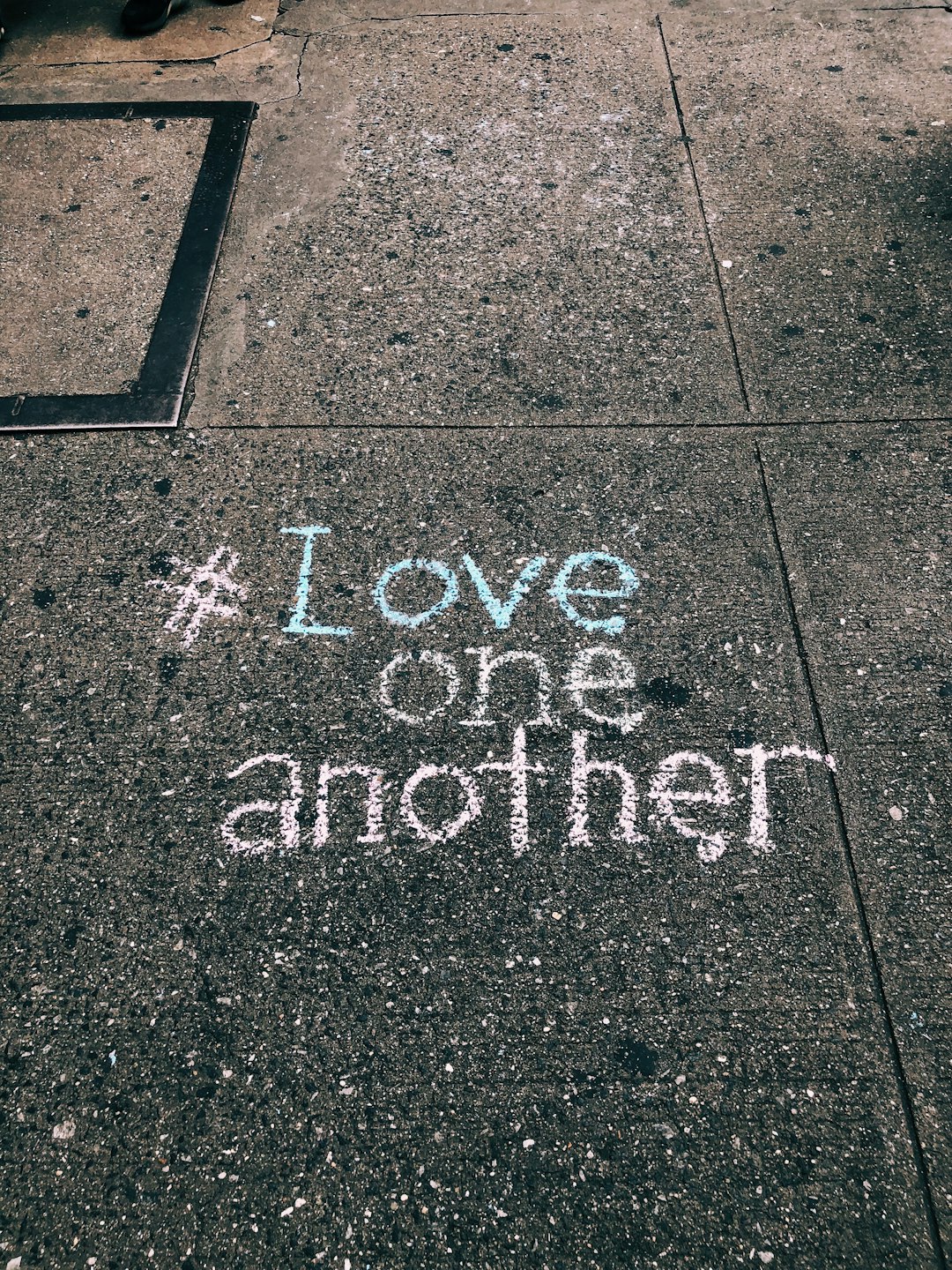 love one another chalk written on concrete floor