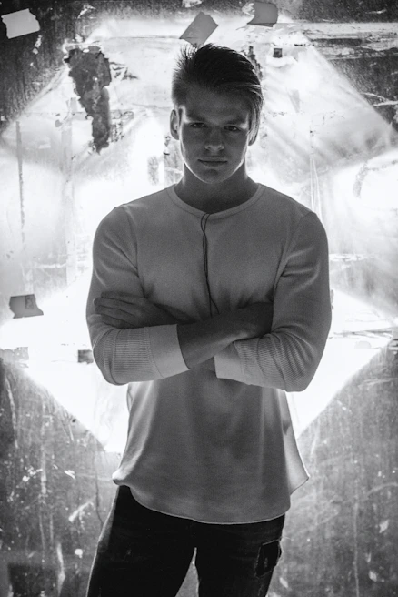 Stylish male model wearing a classic white tee standing in a bright, airy room with soft shadows