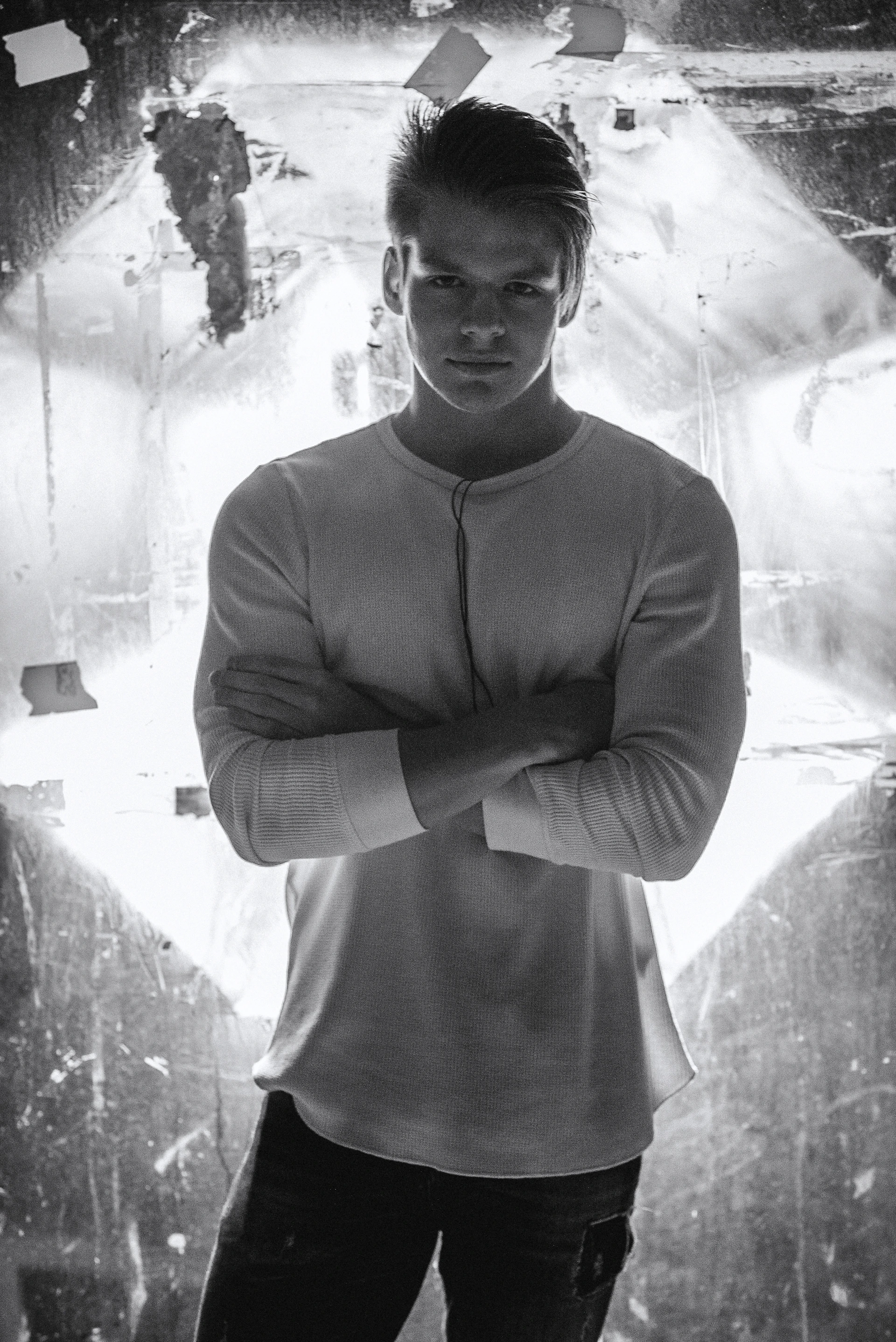 A stylish male model wearing a clean white v-neck t-shirt, standing casually against a soft urban backdrop with natural light highlighting the premium cotton texture.