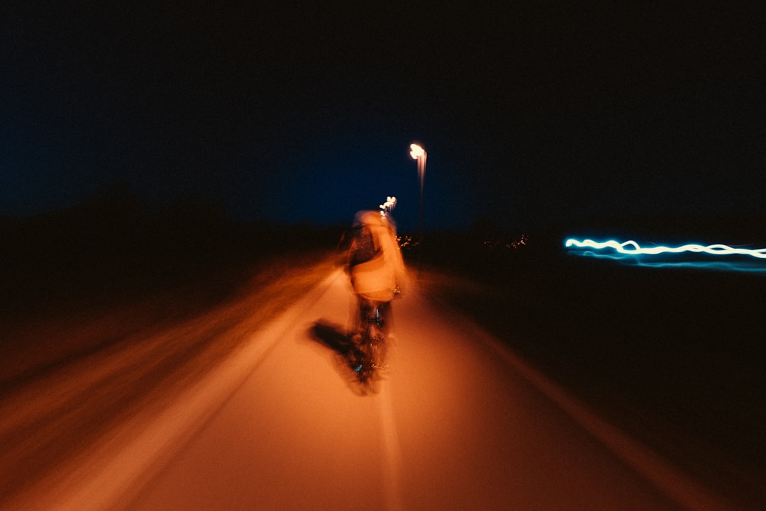 a man riding a skateboard down a street at night, We were biking and I had this idea to just shoot a picture of him, while he is biking and greate blur around him, but the camera shook just too much and there it is. Pretty interesting tho, I kinda like it.