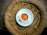 A cup of tea with a rich brown color sits in a white saucer on top of a woven circular mat made from natural fibers.