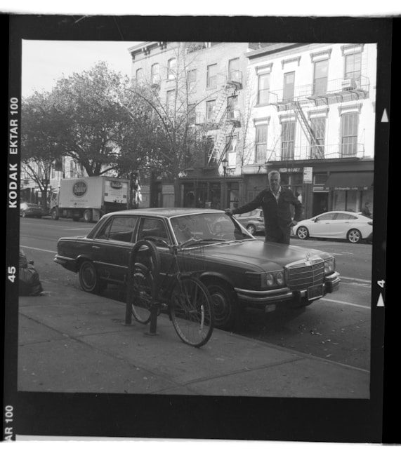 Man standing next to parked 80's Mercedes S-Class car