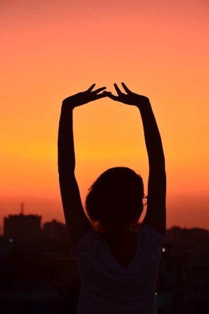 Sunset city skyline with a silhouette of a person stretching in urbanfit activewear on a rooftop.