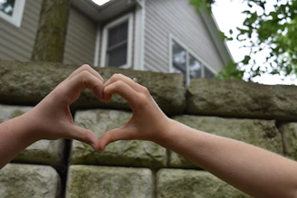 Hands forming a house shape with a heart inside, symbolizing community support and care.