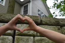 Hands forming a house shape with a heart inside, symbolizing community support and care.