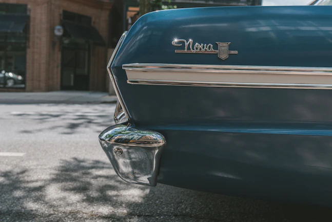 A bright red ’69 Nova with chrome rims parked under a glowing blue and red neon storefront sign.