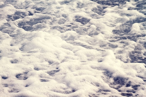 Foamy waves with a mix of white bubbles and darker water below create a textured surface, appearing as if captured at a shoreline.